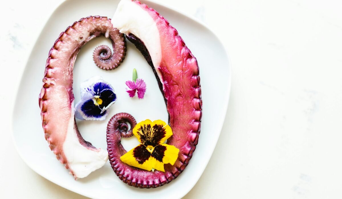 A gourmet dish featuring octopus tentacles and colorful edible flowers on a white plate. — Photo by RDNE Stock project on Pexels