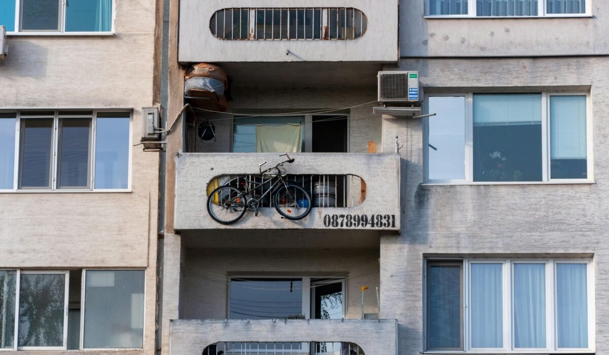 Urban scene of a concrete apartment building with a bicycle on the balcony and visible air conditioning unit. — Photo by wal_ 172619 on Pexels