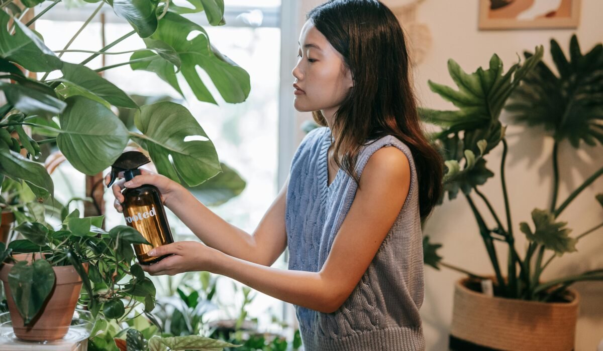 Asian woman using a spray bottle to water houseplants in a cozy indoor setting. — Photo by Sasha Kim on Pexels