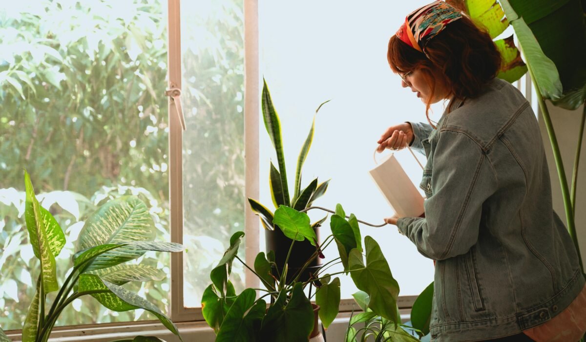 Redheaded woman nurturing green houseplants by a sunlit window indoors. — Photo by Los Muertos Crew on Pexels