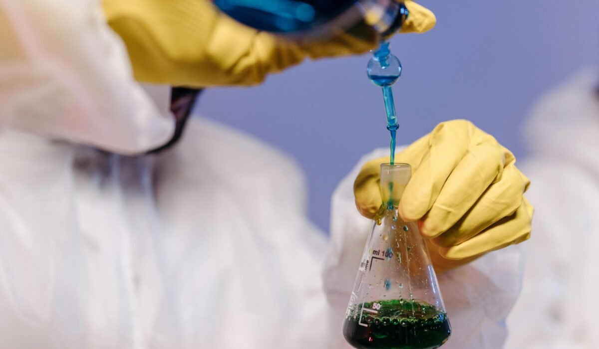 Scientist wearing gloves and lab coat mixing colored liquids in a flask. — Photo by Pavel Danilyuk on Pexels