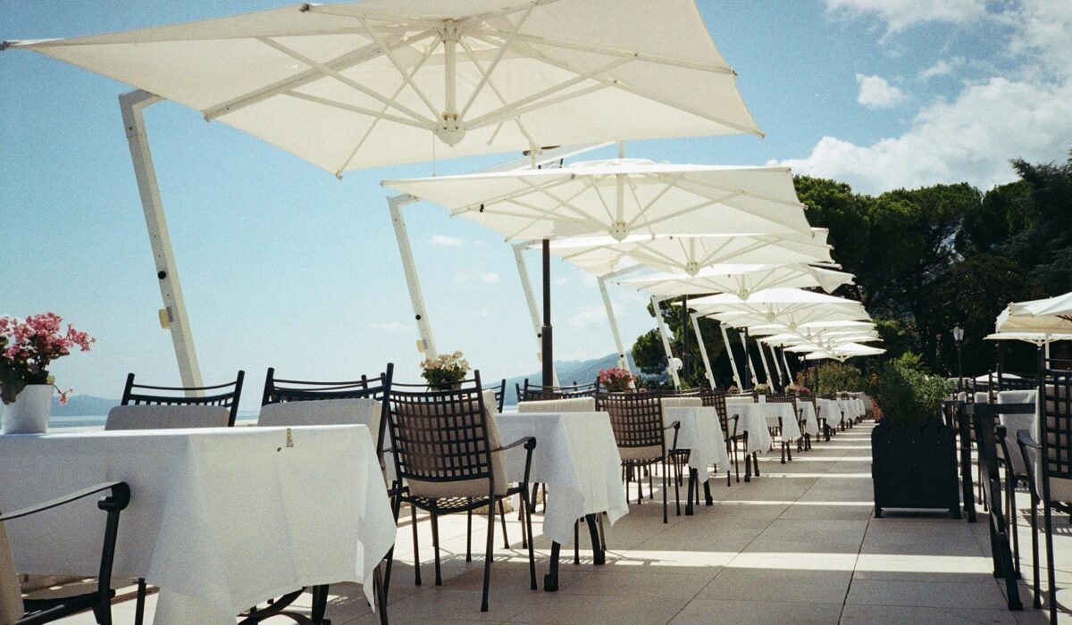 Coastal restaurant terrace with white umbrellas and empty tables, a perfect summer day. — Photo by Zsófia Fehér on Pexels
