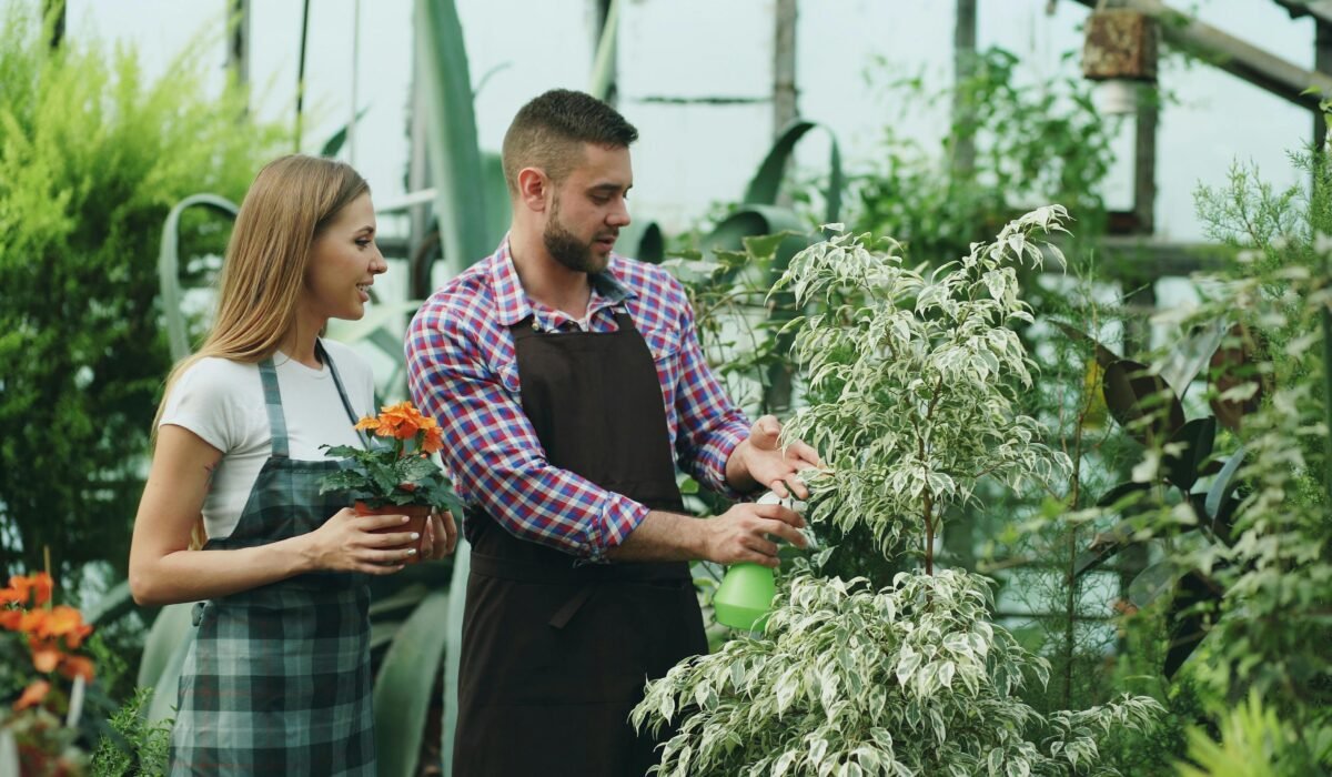 Two gardeners nurturing plants inside a greenhouse, wearing aprons. — Photo by Vitaly Gariev on Pexels