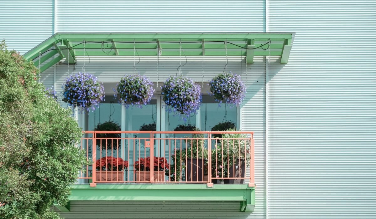 A vibrant balcony adorned with hanging purple flowers and potted plants, adding charm to a modern facade. — Photo by Kai-Chieh Chan on Pexels